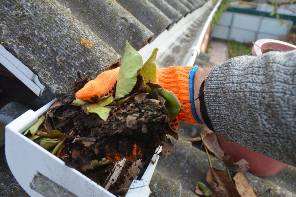 Man picking up the dirt and leaves in the gutter — Handyman in Sussex Inlet, NSW