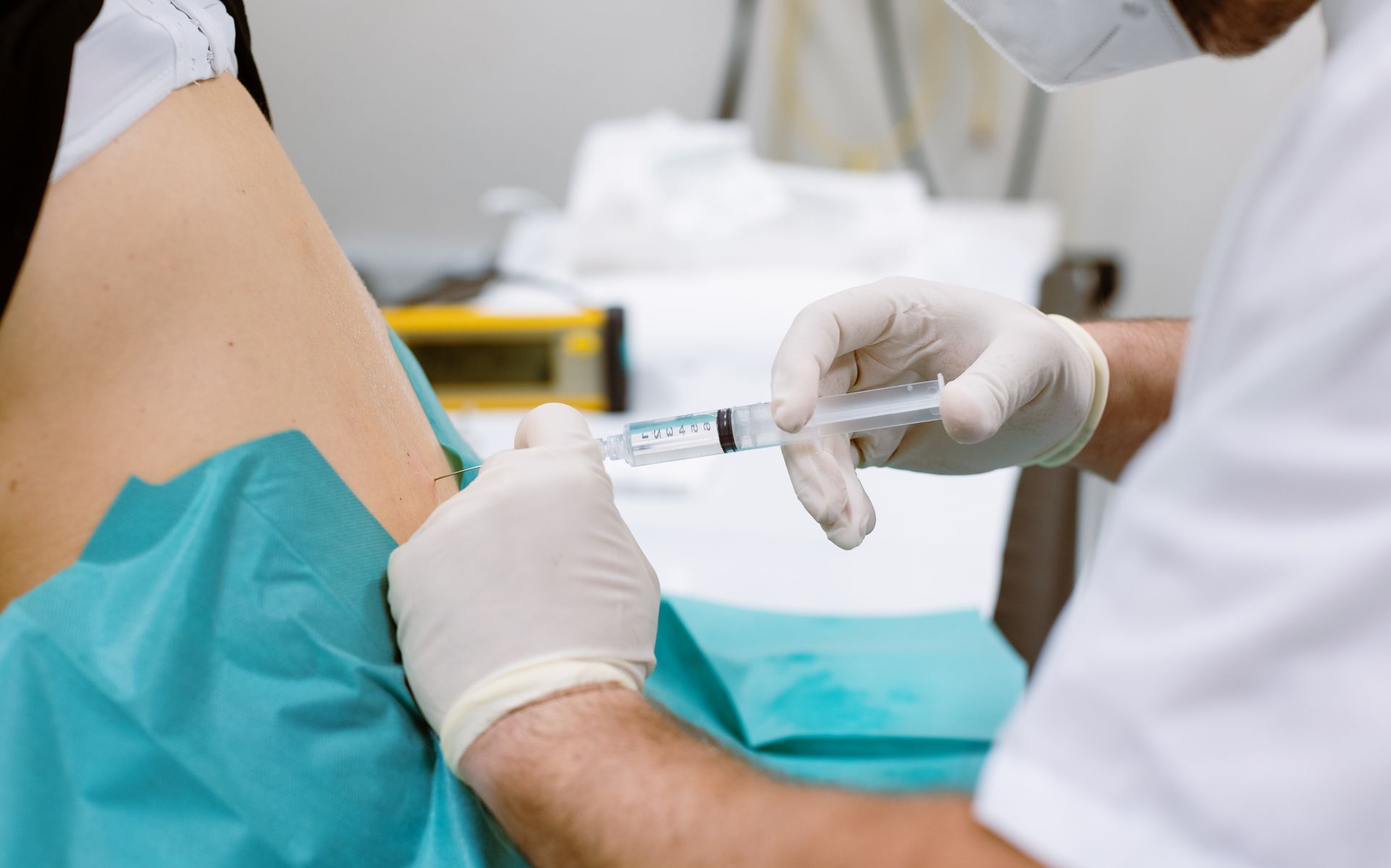 Medizinisches Fachpersonal injiziert einem Patienten in einer Klinik einen Impfstoff in den Oberarm.
