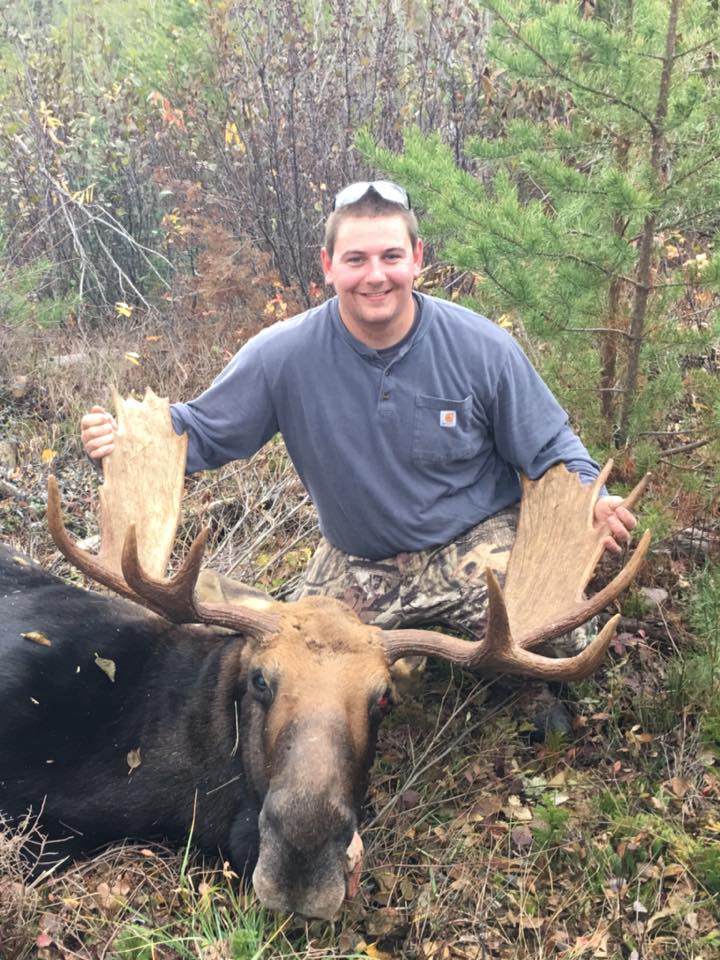 A man is standing next to a moose in the woods.