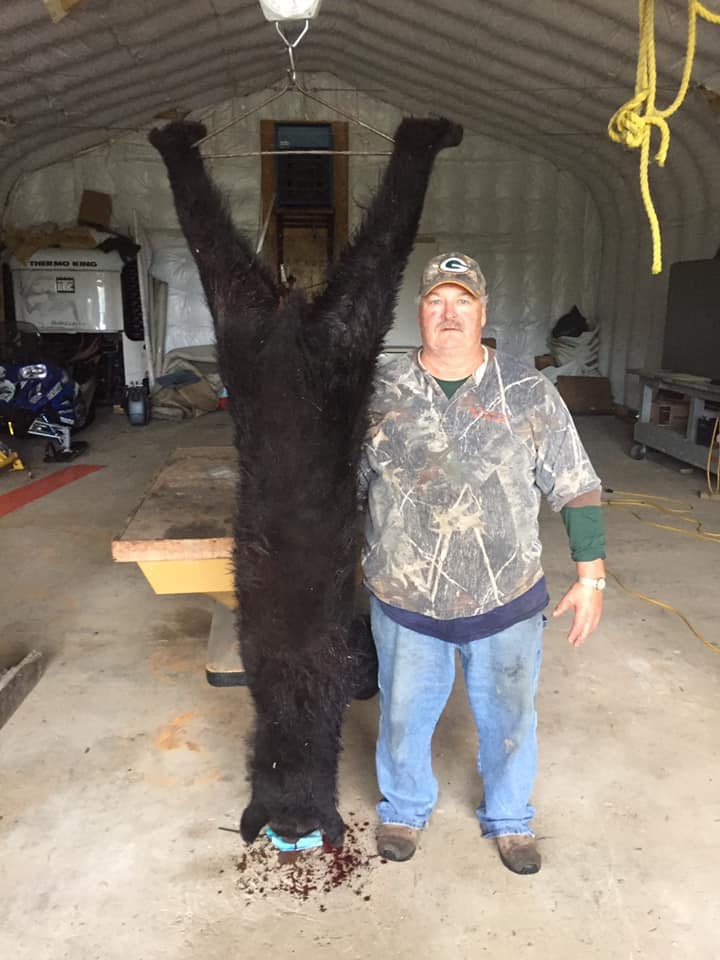 A man is standing next to a large black bear in a garage.