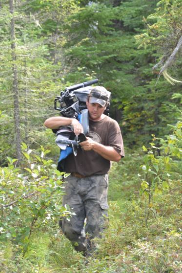 A man is carrying a motor through the woods.