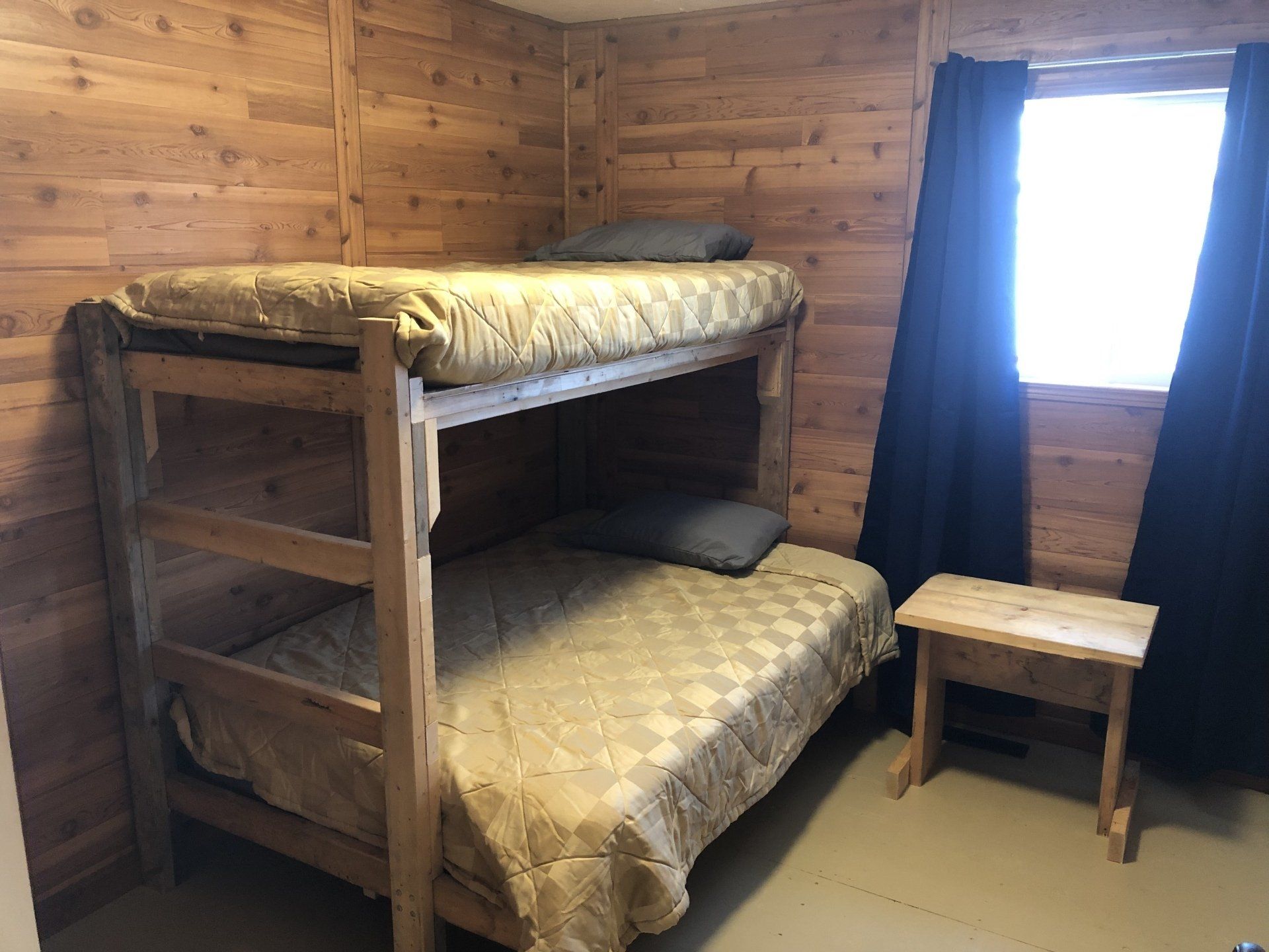 A bunk bed is sitting in a wooden room next to a window.
