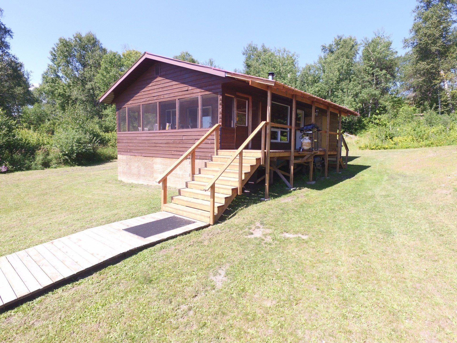 A wooden house with stairs leading up to it is in the middle of a grassy field.