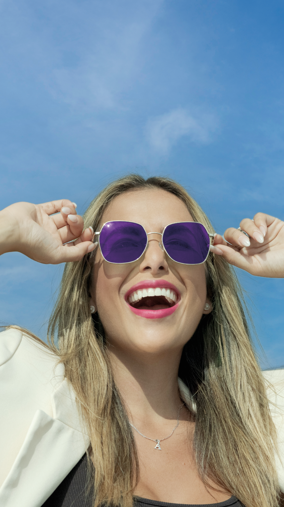 Una mujer lleva lentes o gafas de sol de color morado y sonríe.