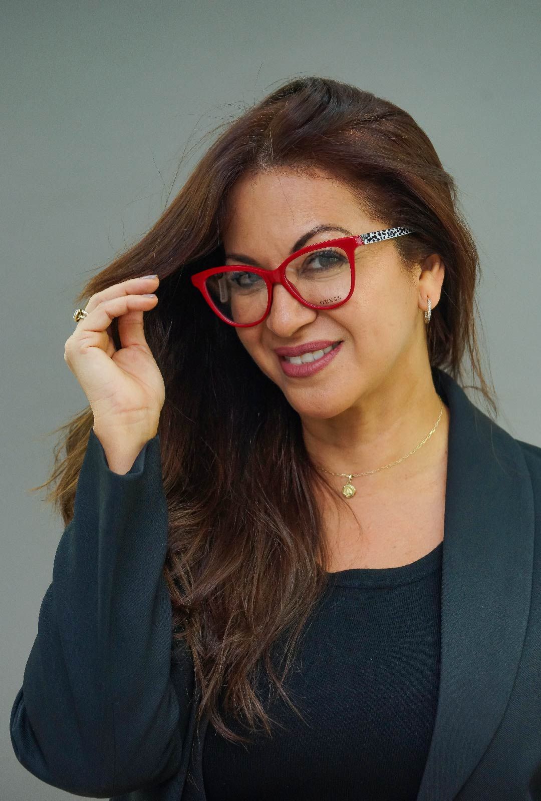 Una mujer que lleva lentes rojas y una chaqueta negra está sonriendo.