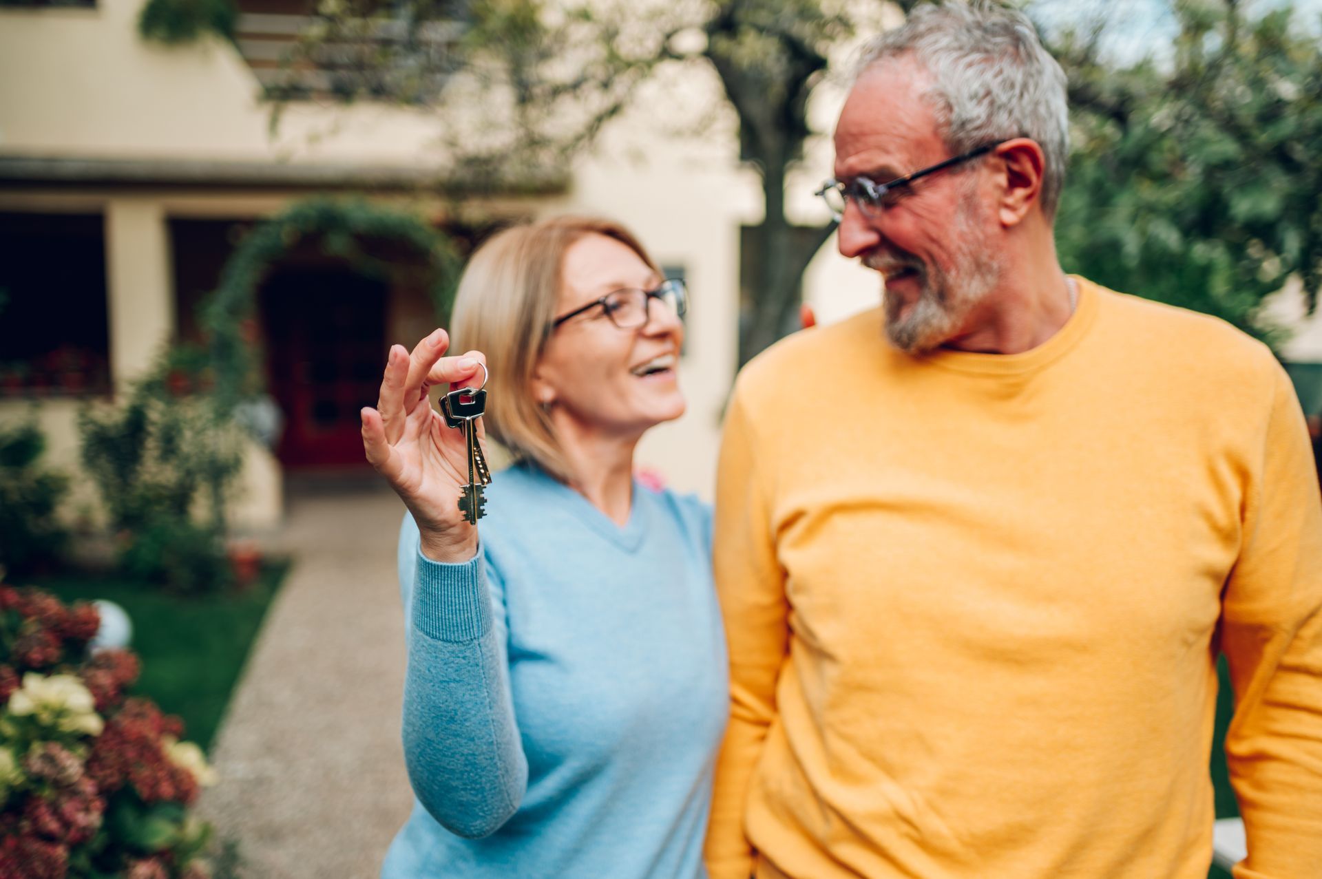 A man and a woman are standing in front of a house holding keys.