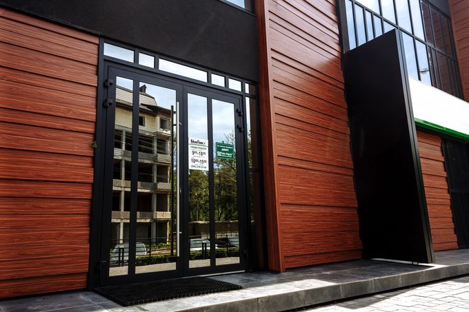 Ingresso moderno dell'edificio con pareti rivestite in legno e porta a doppia anta in vetro con telaio in metallo nero, all'esterno.