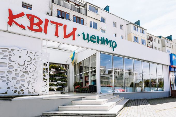 Esterno del negozio di fiori Kvity-tsentr, caratterizzato da una grande insegna rossa e verde sopra una moderna vetrina con vetrate.