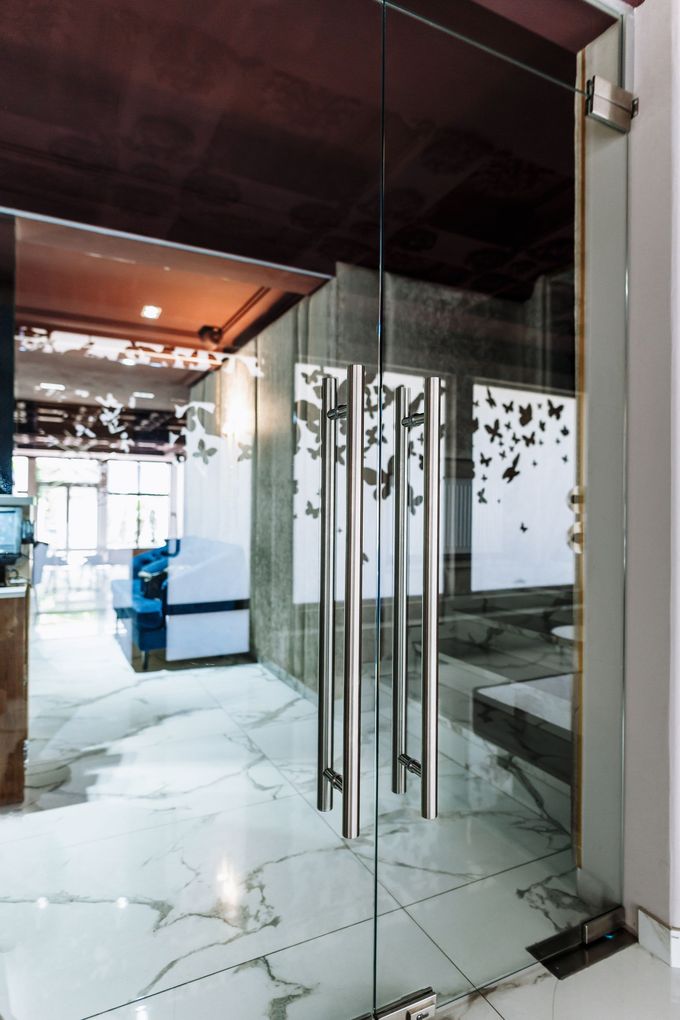 Una porta a vetri con alte maniglie in metallo argentato, che si apre su un interno luminoso con pavimenti in marmo bianco e decorazioni a forma di farfalla.