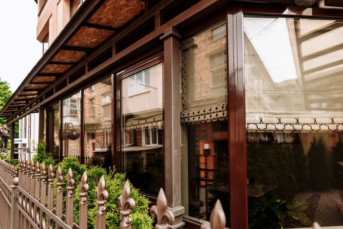 Un'area salotto esterna con patio, racchiusa da una struttura in legno con ampie vetrate, vista da dietro una recinzione metallica.