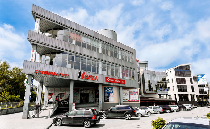 Un moderno edificio commerciale a più piani con facciate e insegne in vetro, dotato di un parcheggio esterno antistante.