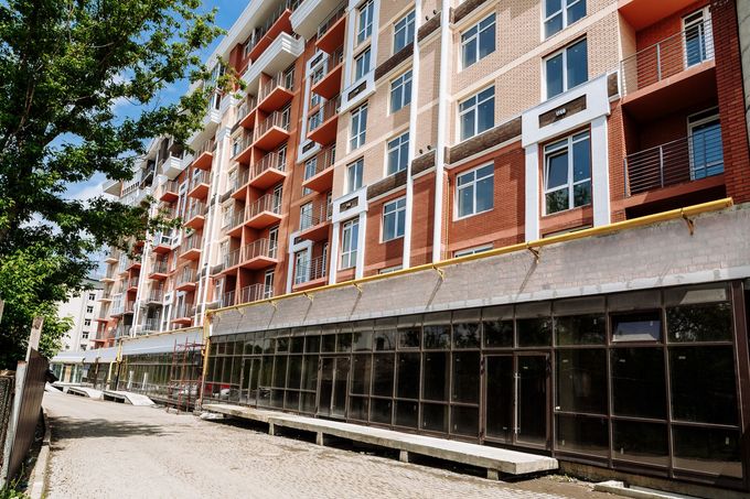 Un condominio a più piani con dettagli in mattoni rossi e un moderno piano terra con facciata in vetro, sotto un cielo azzurro.