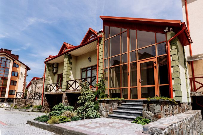Una veduta dal basso di un edificio moderno con ingresso vetrato, dettagli in pietra e tetto di tegole rosse, sotto un cielo azzurro.