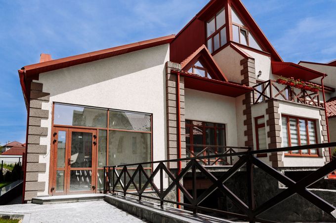 Una casa moderna a due piani con facciata in stucco di colore chiaro, dettagli angolari in pietra, tetto rosso e ringhiera del portico in legno.