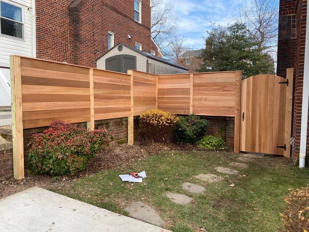 Wooden fence with gate in front yard, brick building in background.