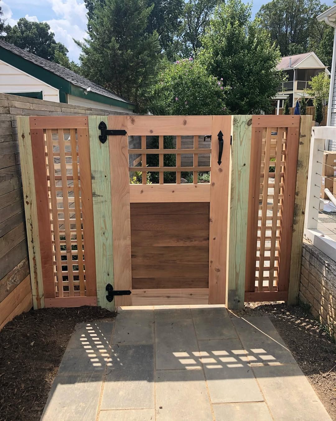 Wooden gate with lattice side panels and a brick pathway, surrounded by greenery.