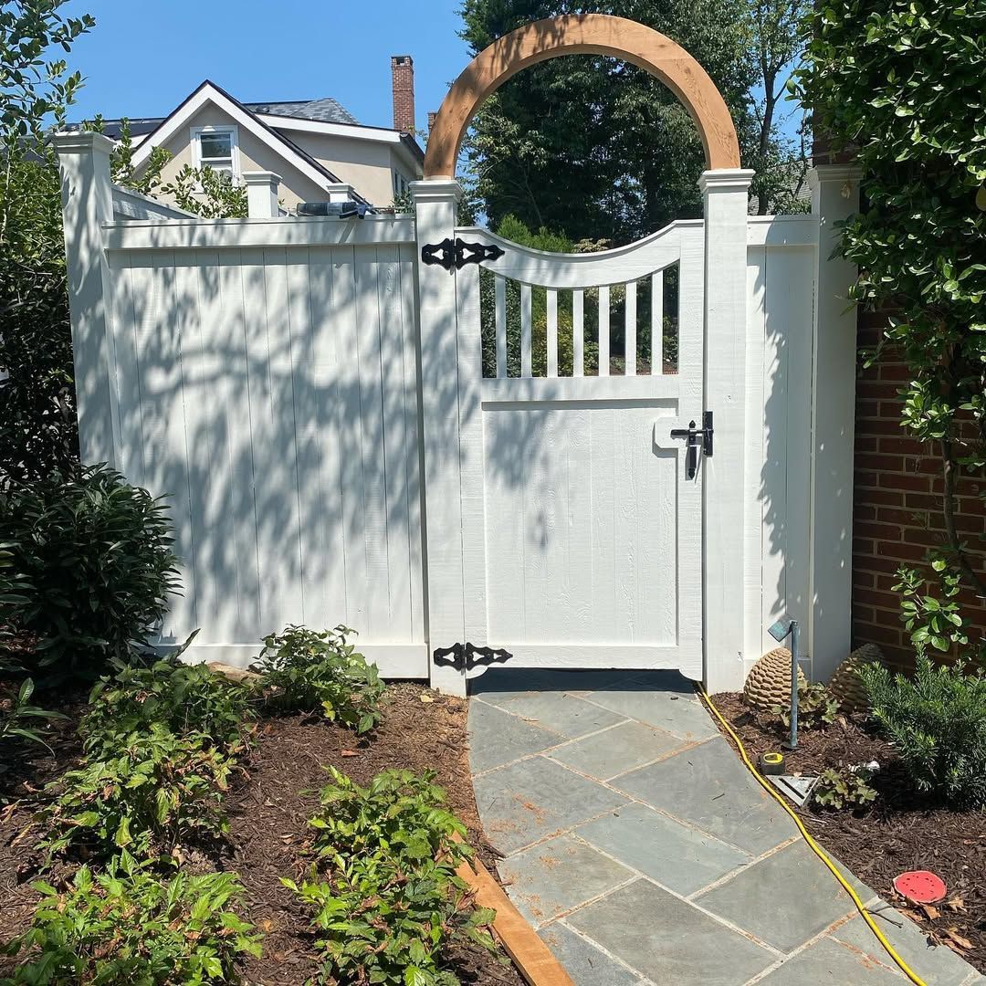 White picket fence with gate, arched wooden top, slate path.