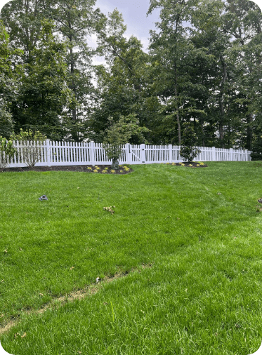 White picket fence surrounds a green lawn with trees in the background.