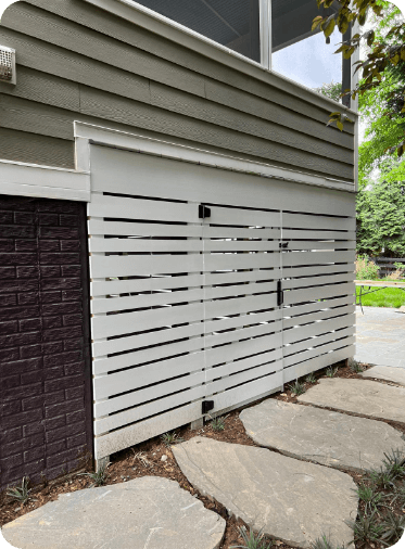 White horizontal slatted storage unit built into the side of a building, surrounded by stone pavers and landscaping.