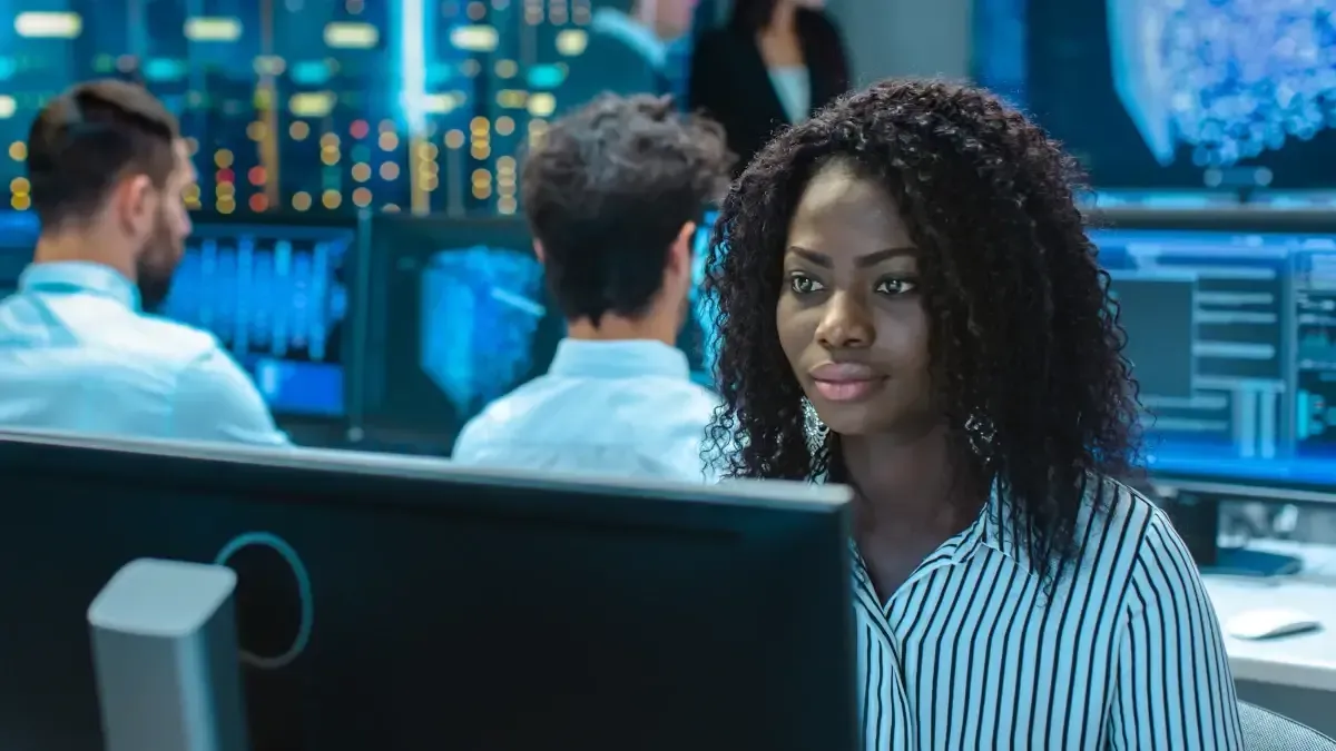 Woman in striped shirt working on a computer in a tech-filled office.