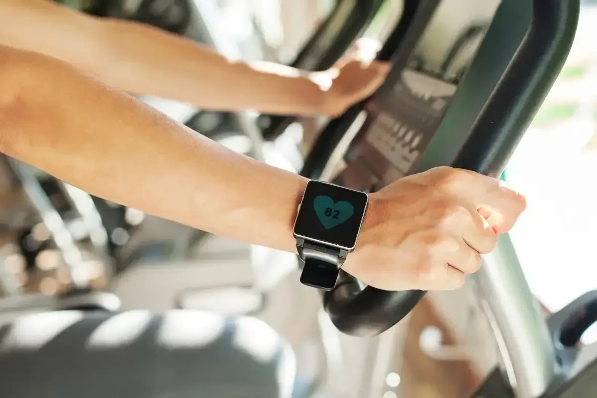 Person wearing a smartwatch while using an elliptical machine, displaying a heartbeat icon.
