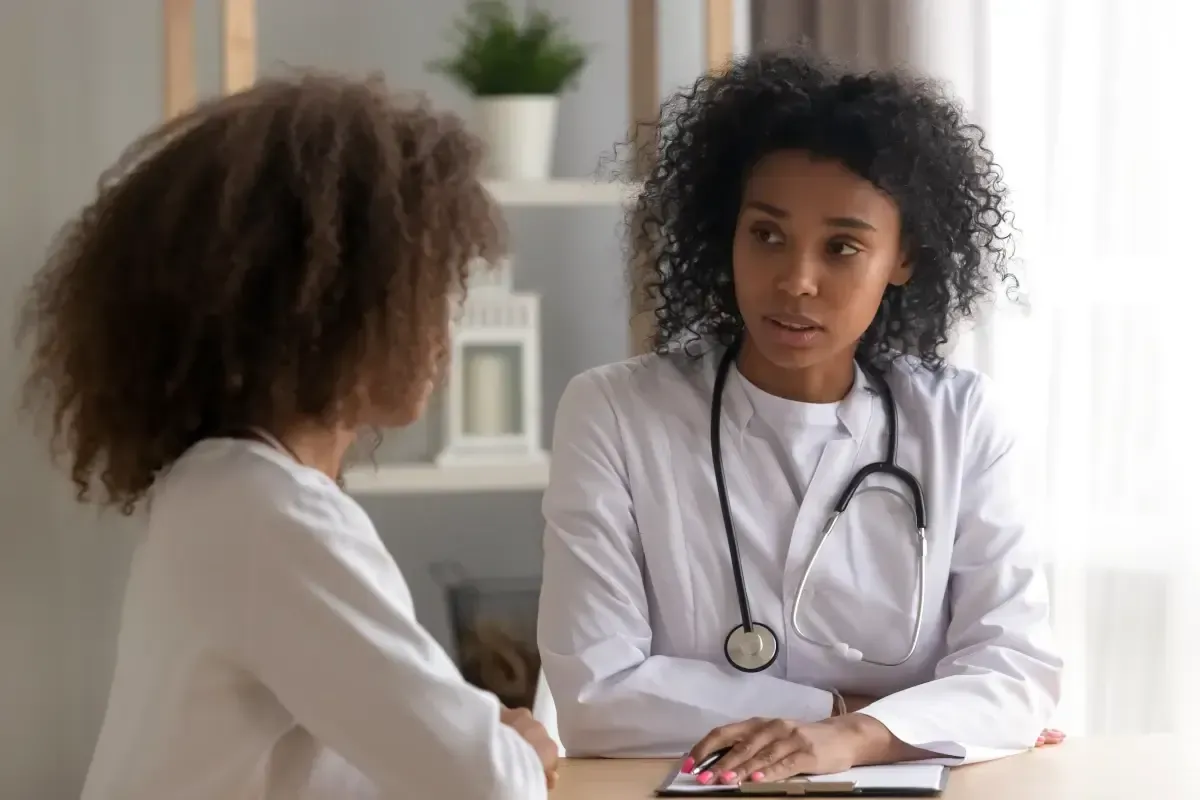 Foto de uma médica negra atendendo uma garota jovem em consultório.