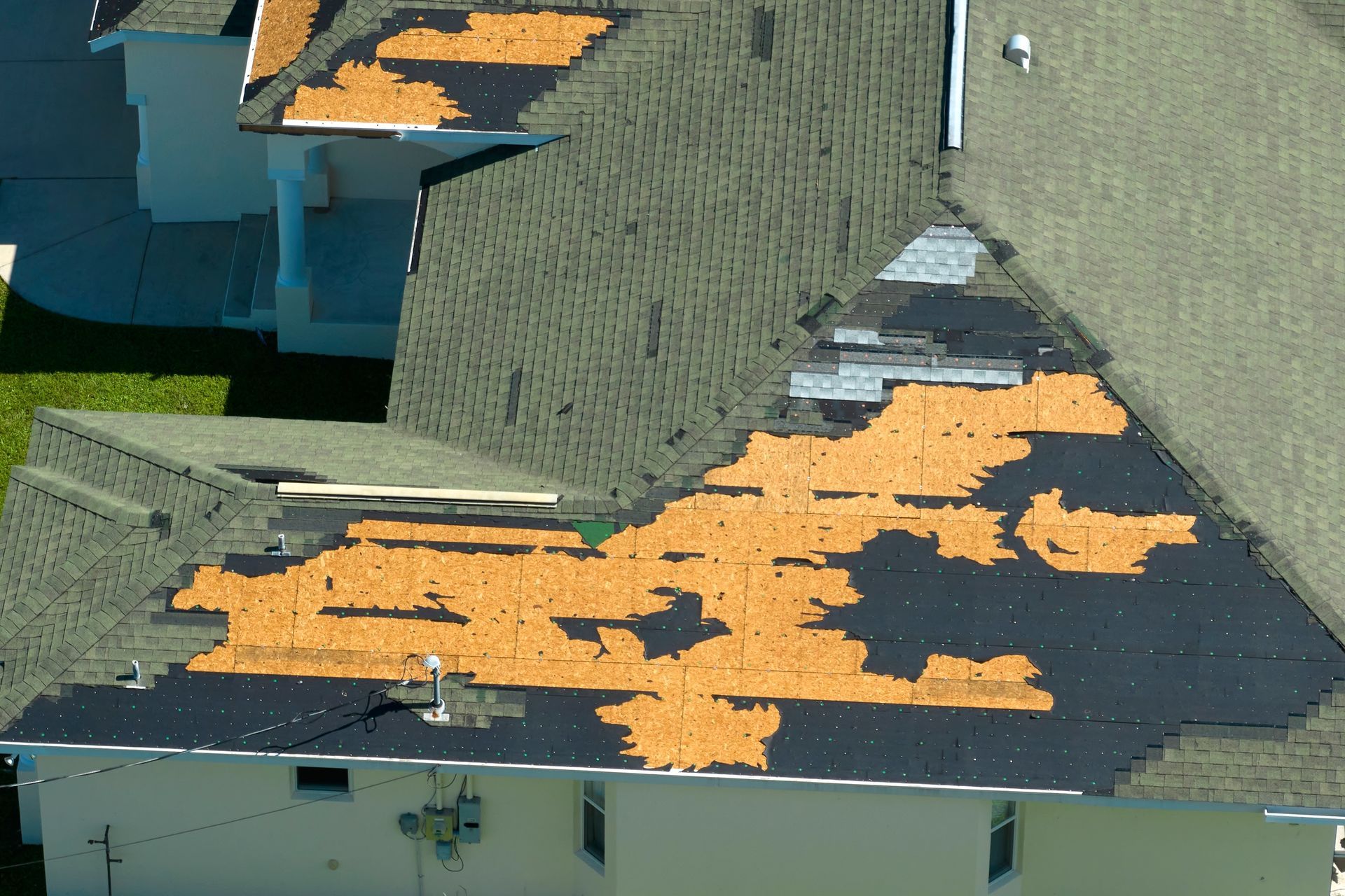 Damaged asphalt shingle roof, with missing patches exposing underlayment.