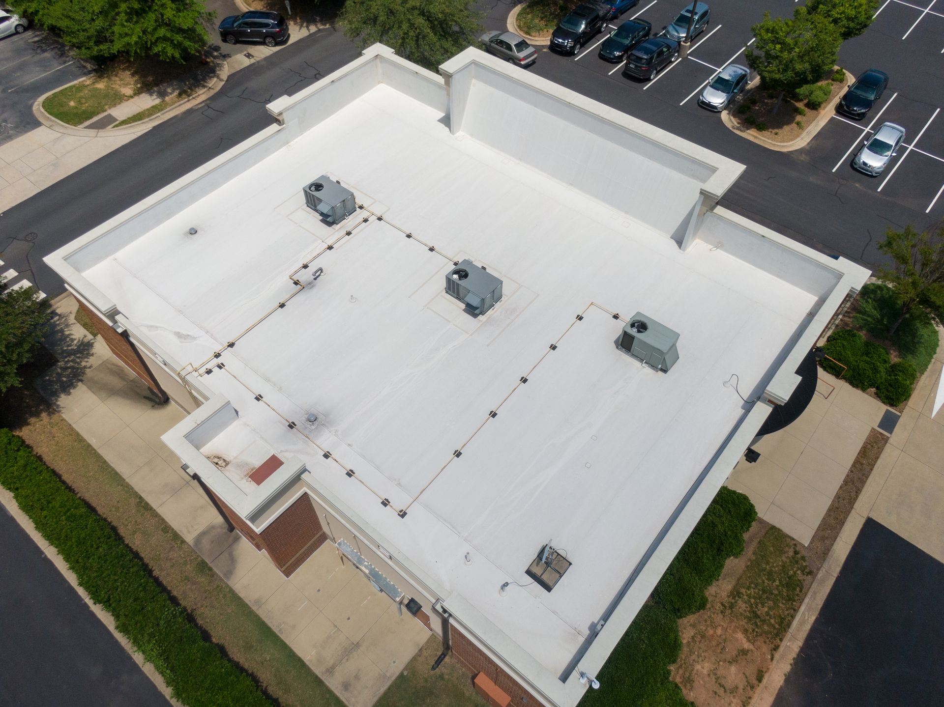 Aerial view of a flat white commercial roof with HVAC units and a parking lot in the background.