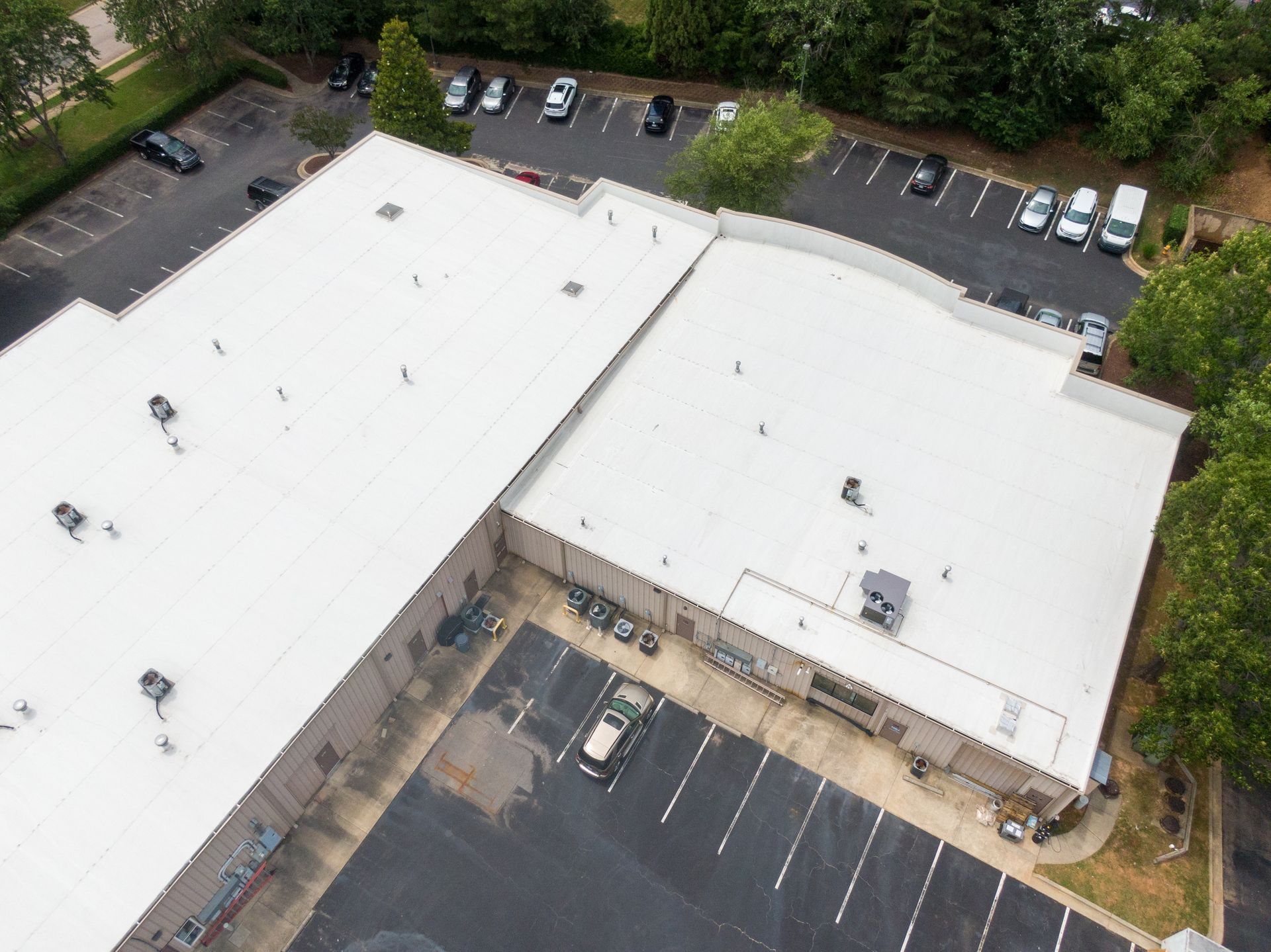 Aerial view of a flat white commercial roof with HVAC units and a parking lot in the background.