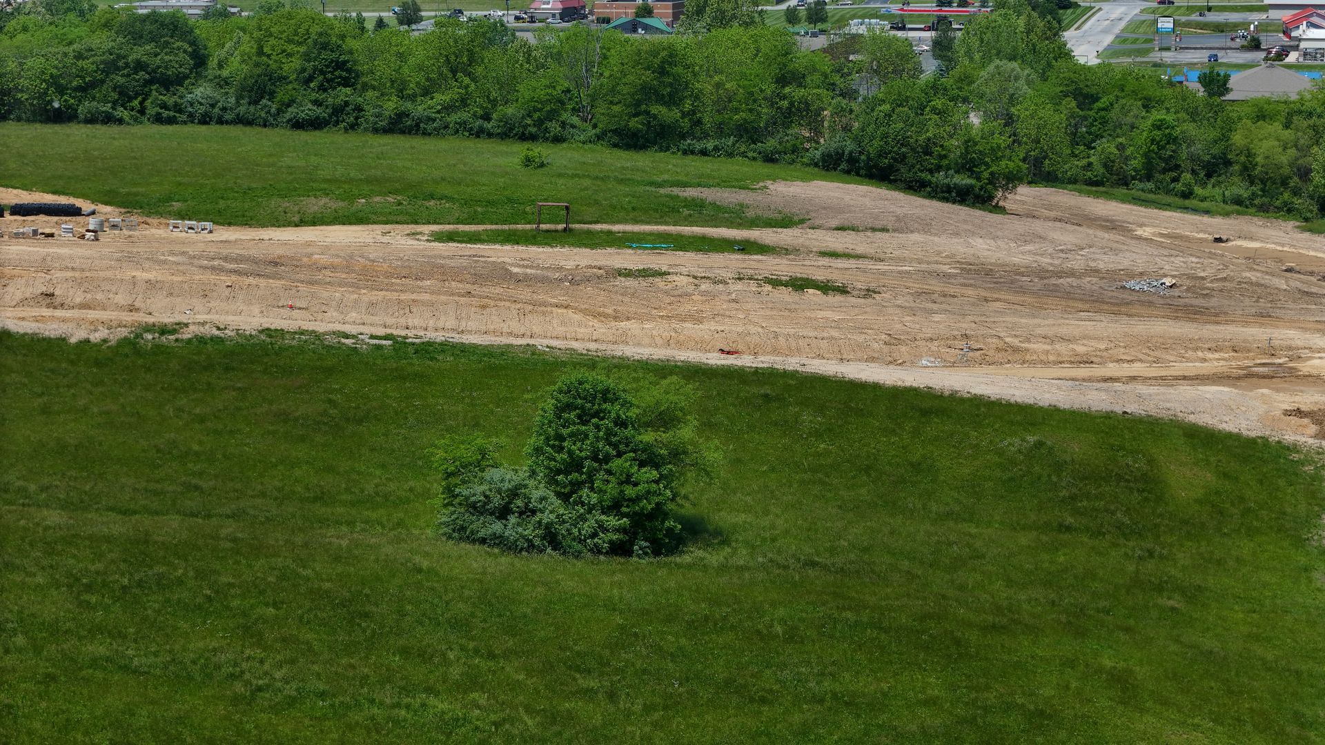 An aerial view of a large grassy field with a small tree in the middle.