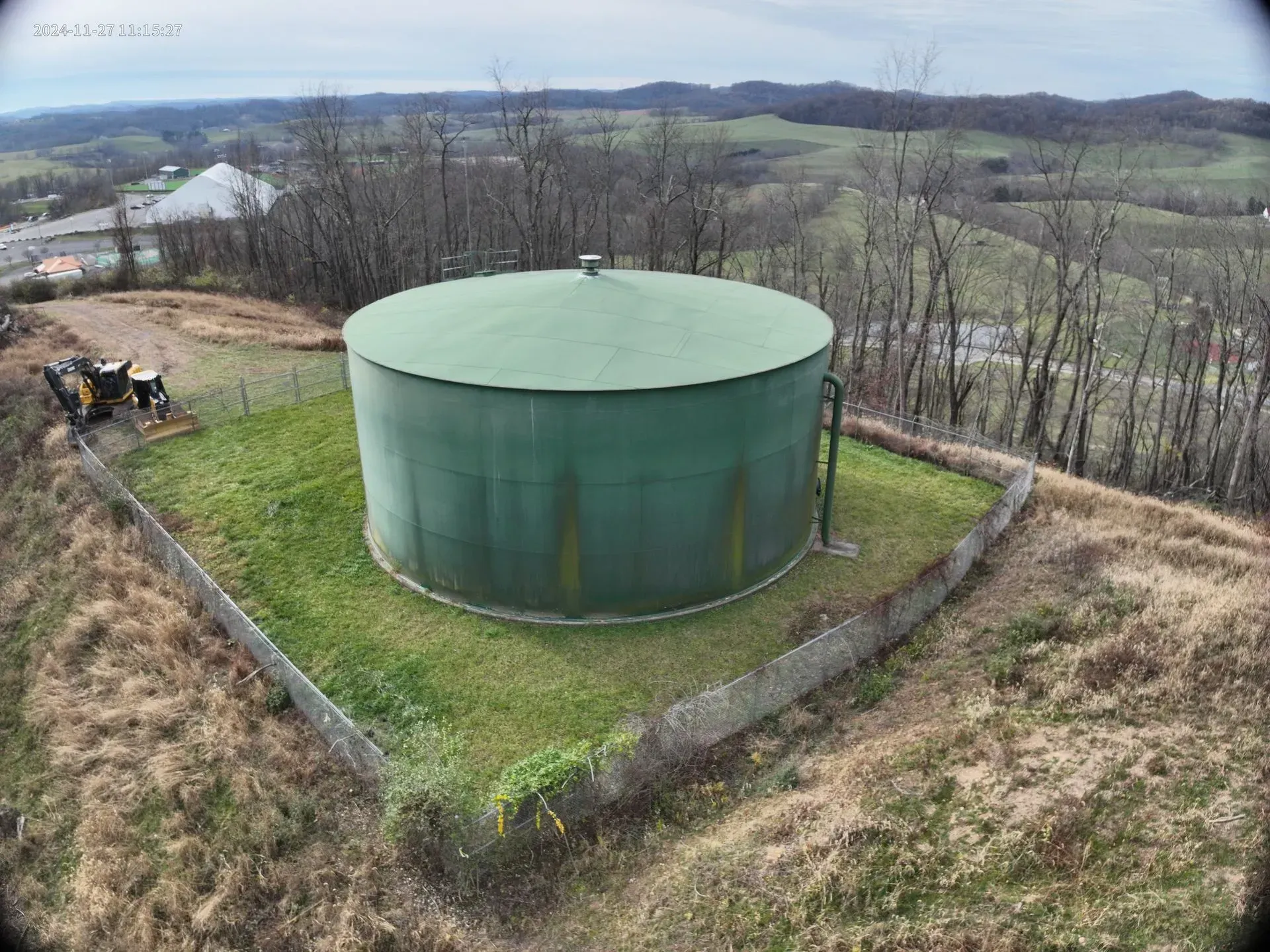 An aerial view of a large green water tank on top of a grassy hill.