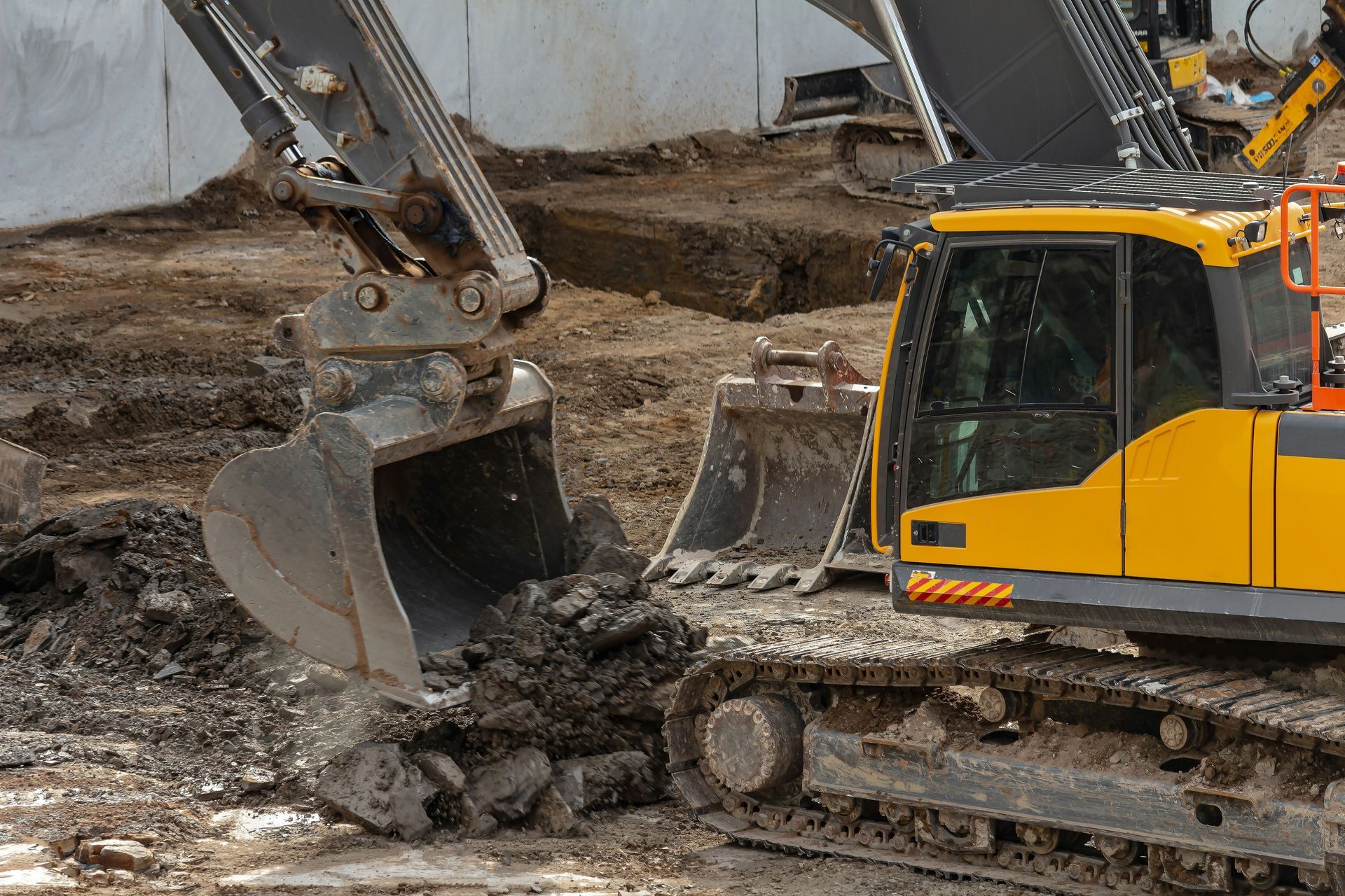 Yellow excavator with bucket scooping dirt at a construction site.