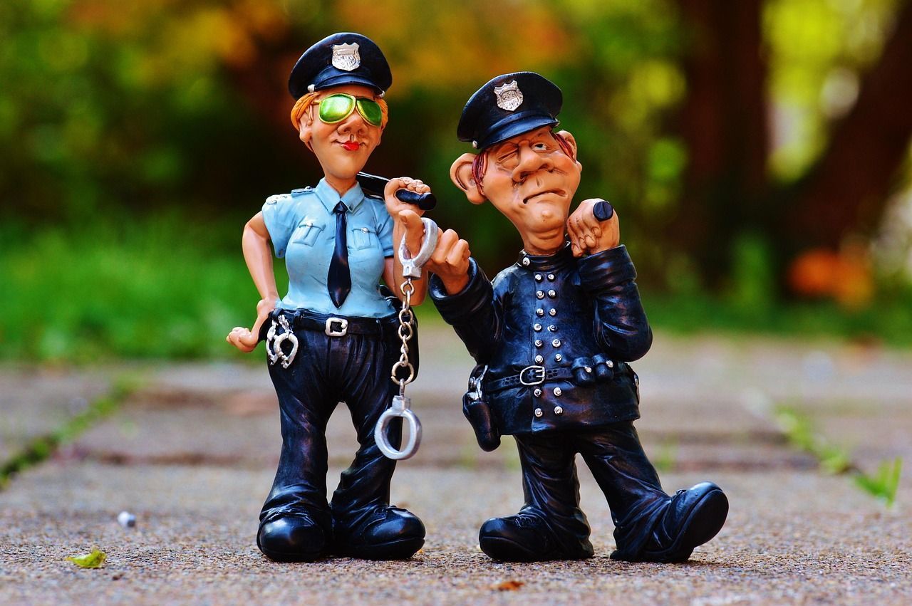 Two cartoon police officers standing outside; one holding handcuffs, the other leaning, looking tired.
