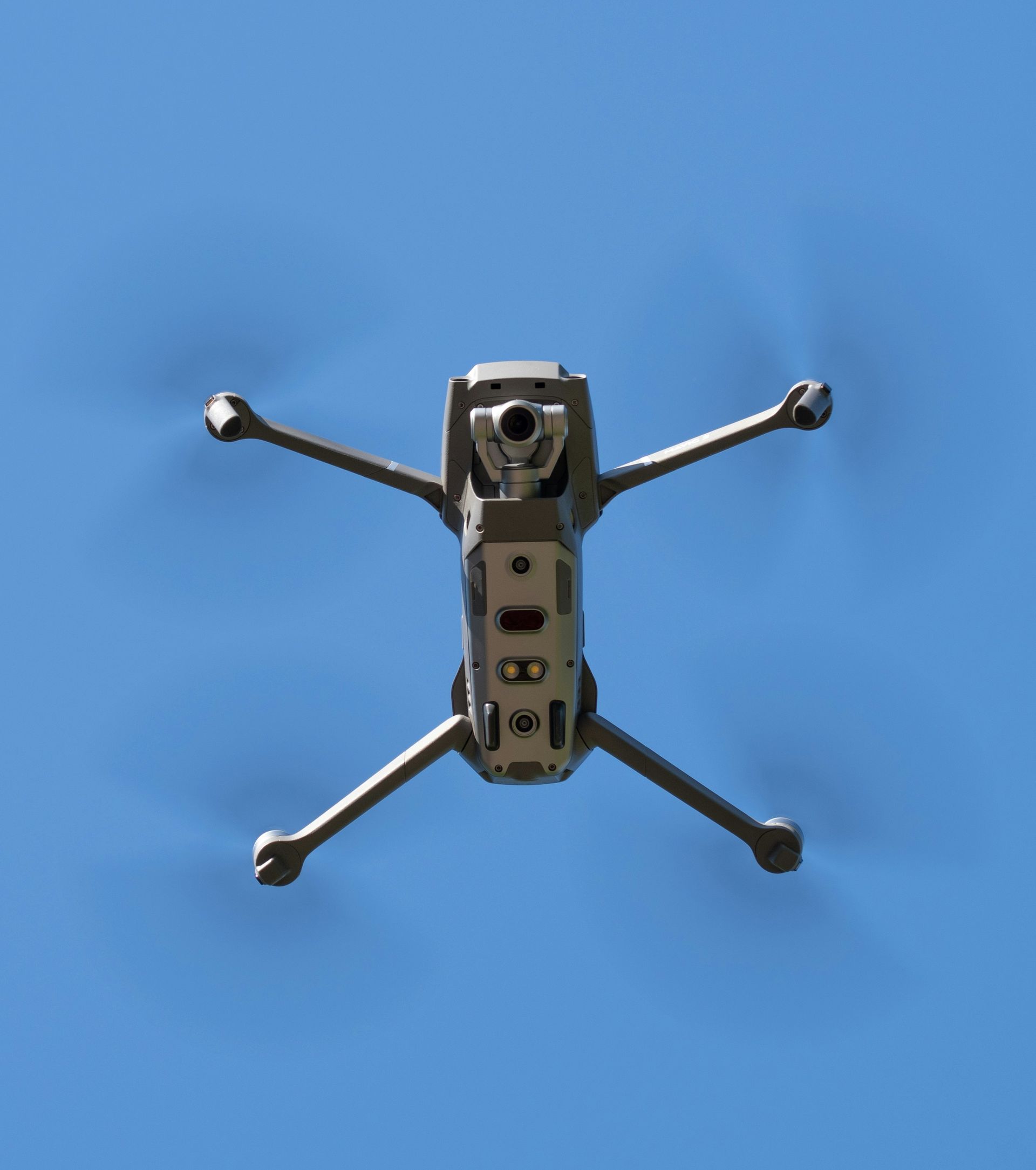 Drone with spinning propellers against a blue sky.