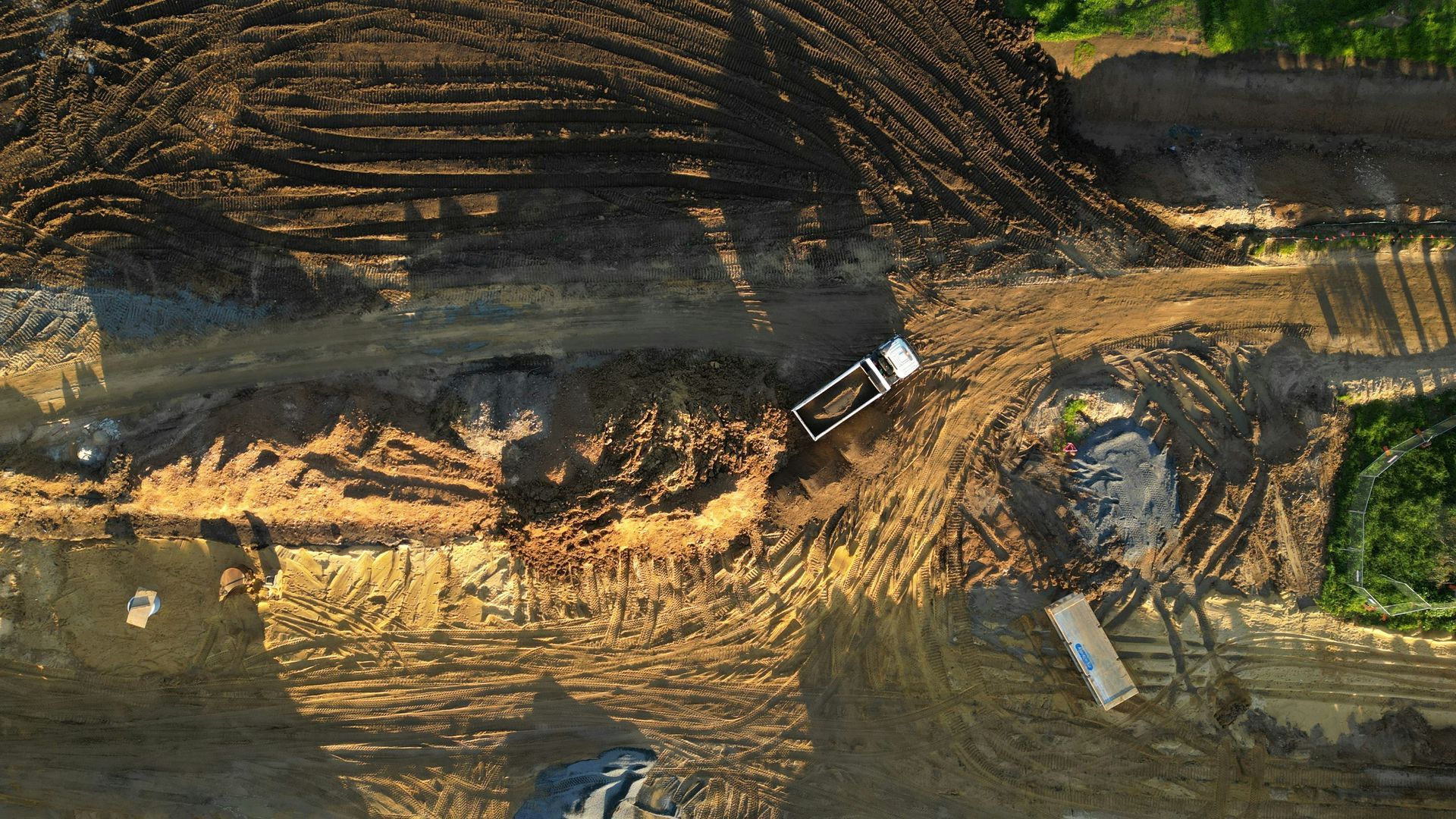 Overhead view of a construction site: dump truck on a dirt road, brown earth, and green vegetation.
