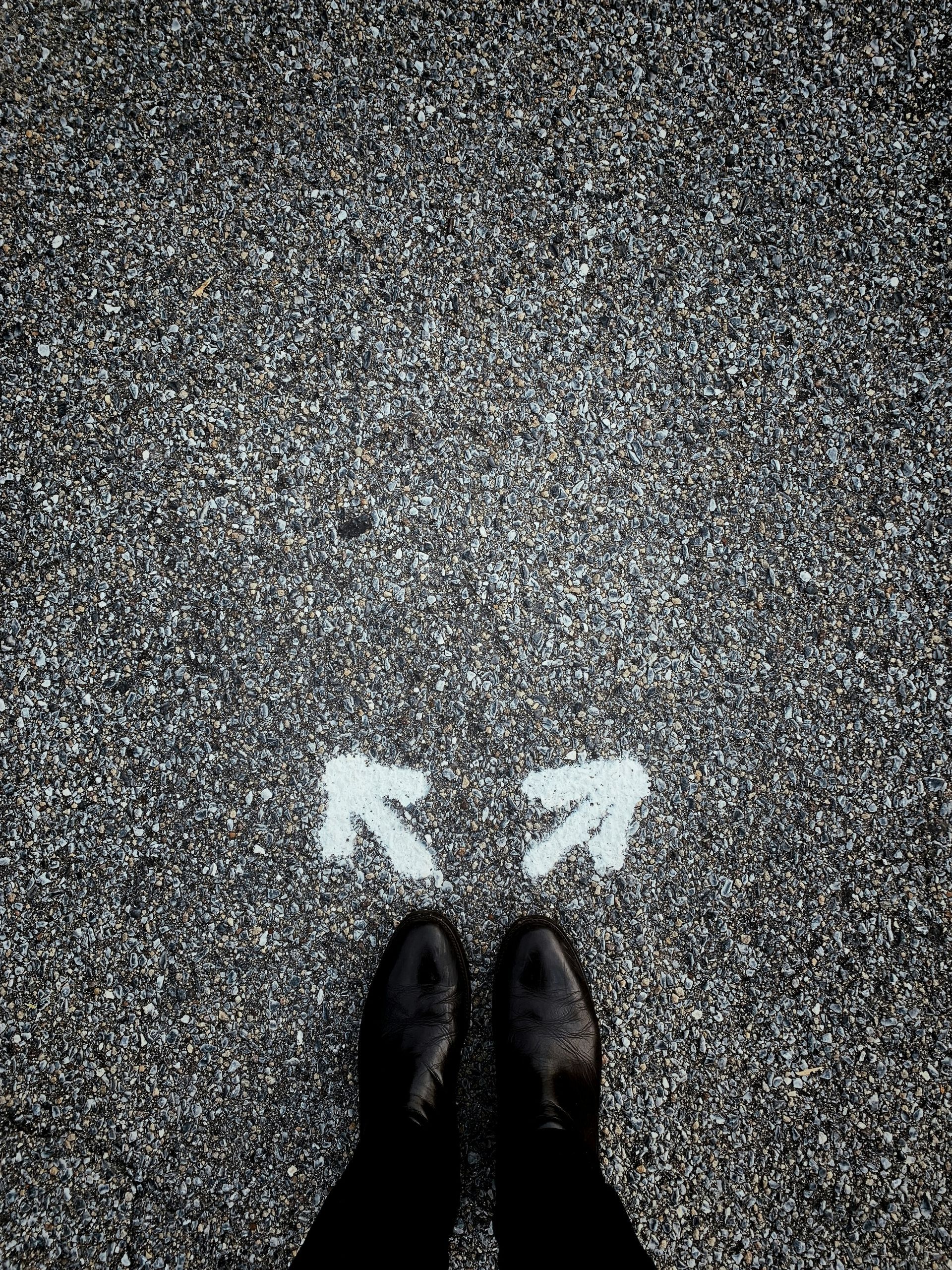 A person is standing in front of two white arrows painted on the ground.