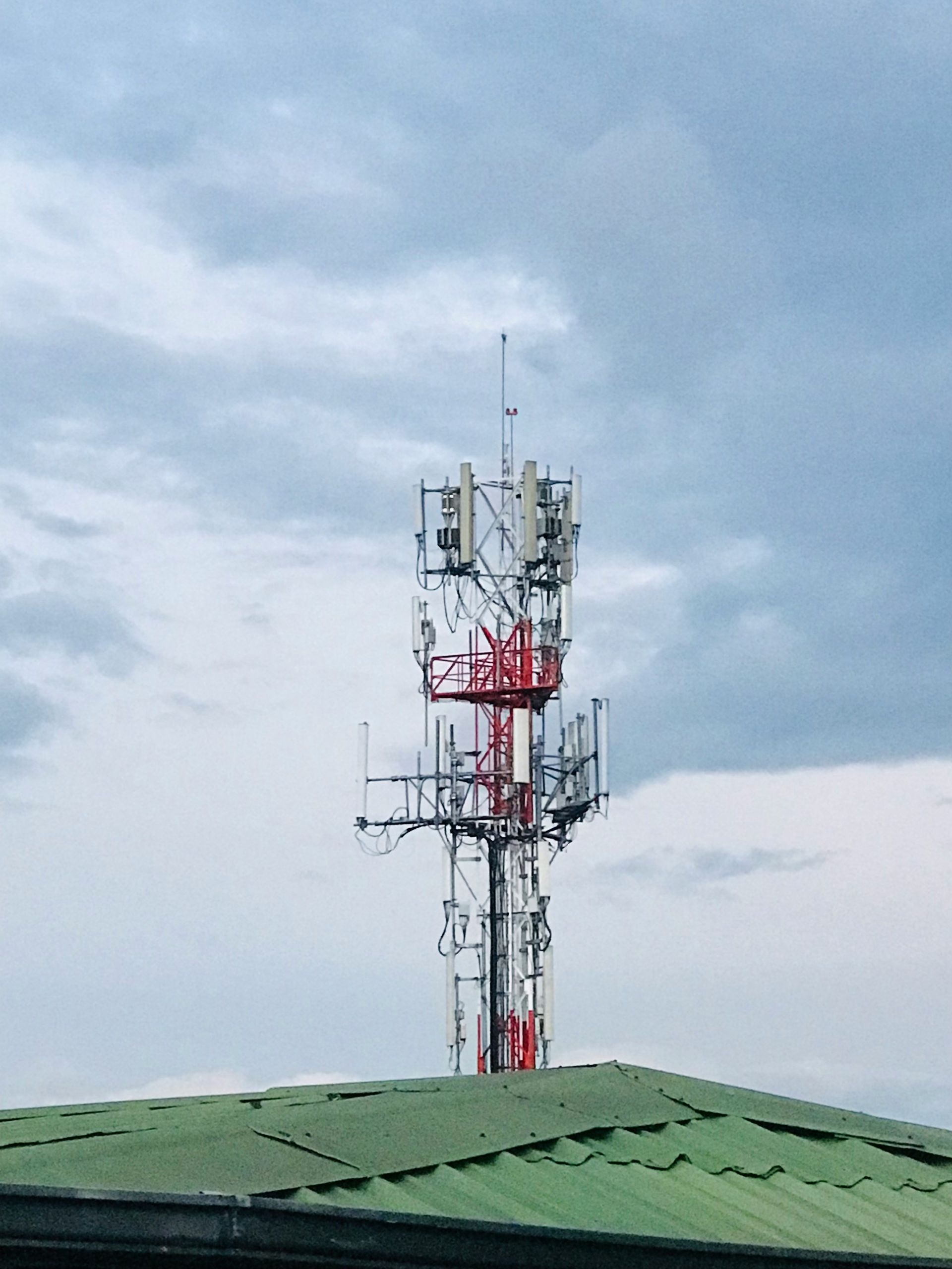 Cell phone tower against a cloudy sky, atop a green roof.