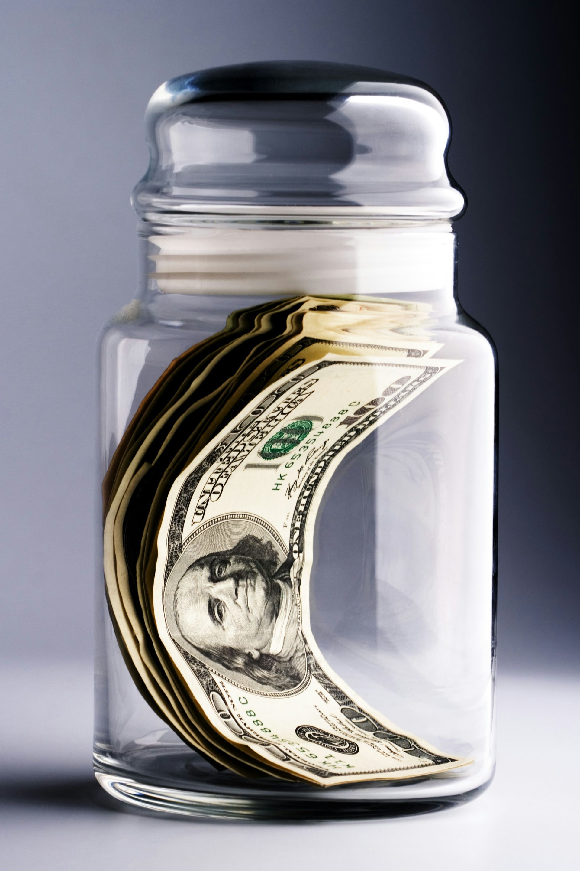 A glass jar filled with a stack of 50 dollar bills