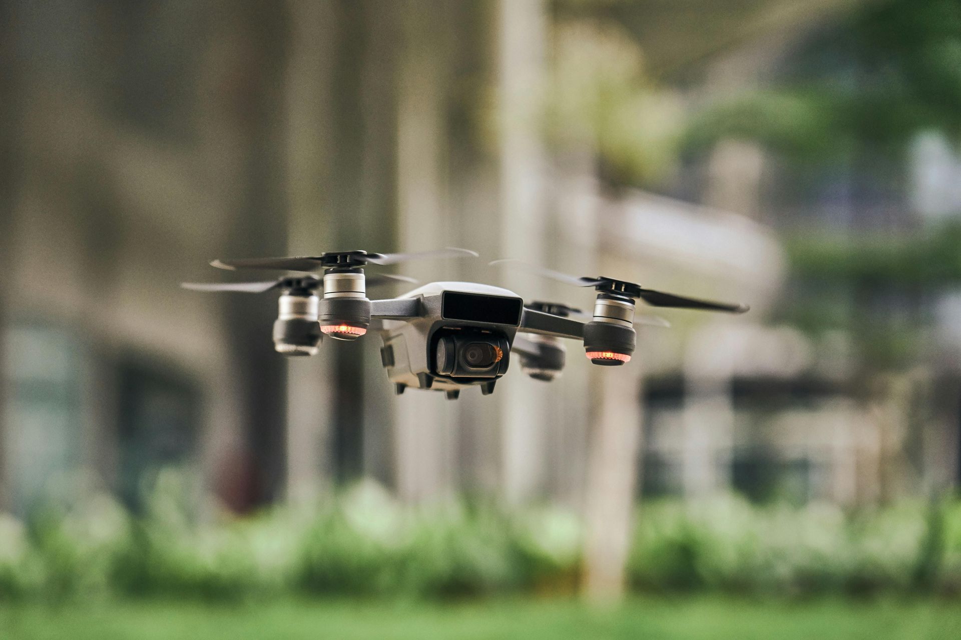 A drone is flying over a field with trees in the background.