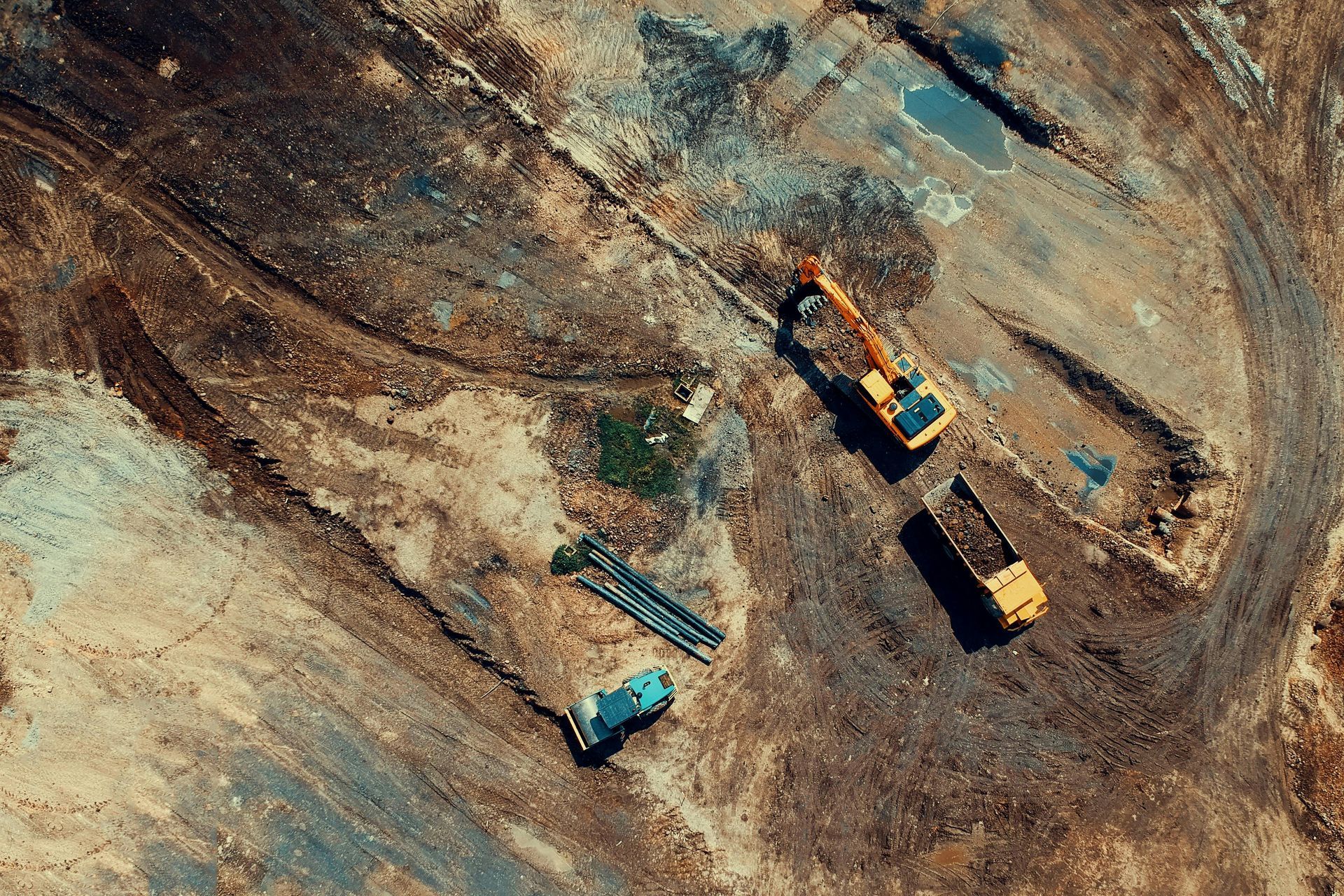 Aerial view of construction site: excavator, dump truck, and materials on brown earth.