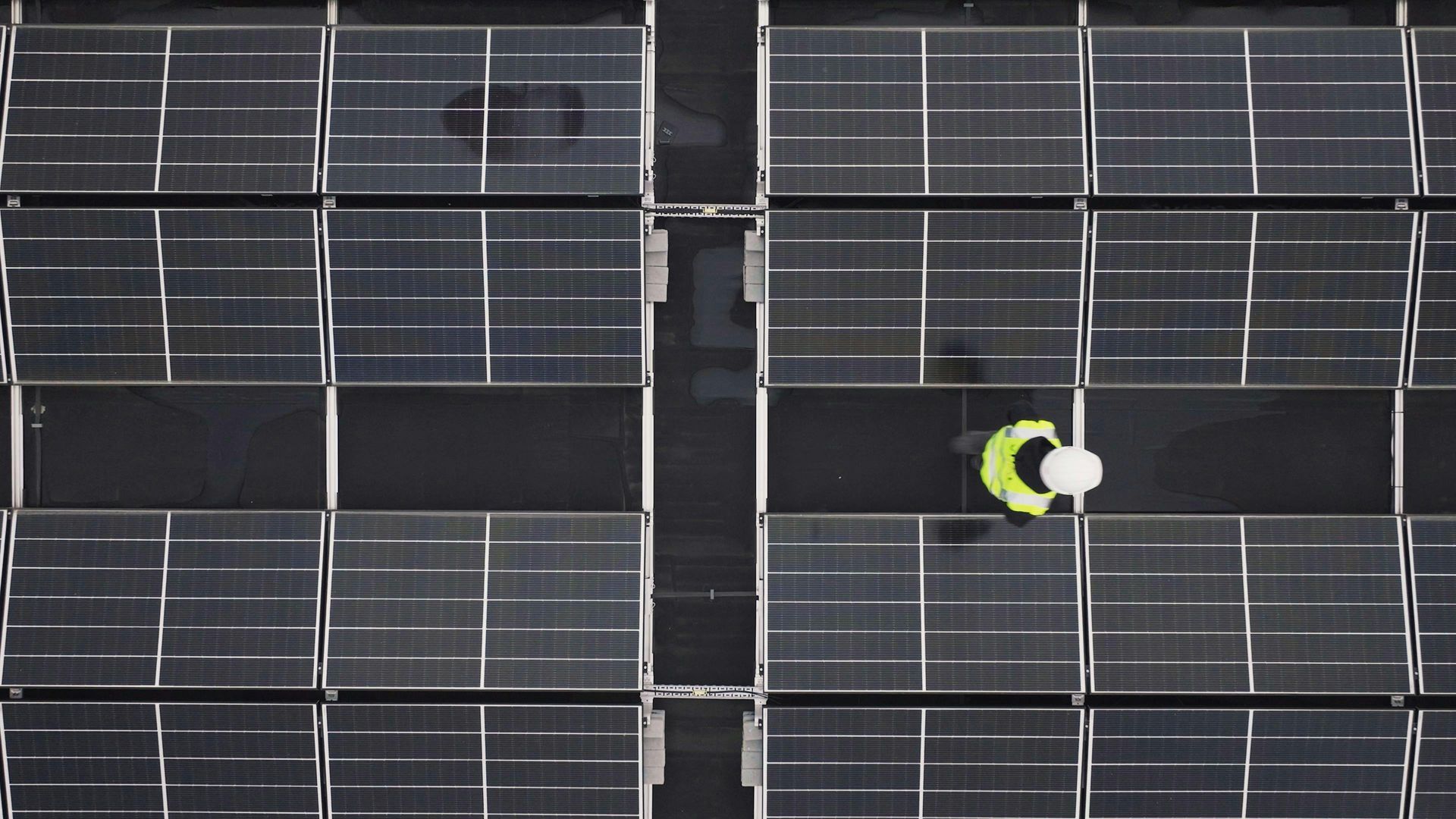 Worker in safety vest and hardhat inspecting solar panels.