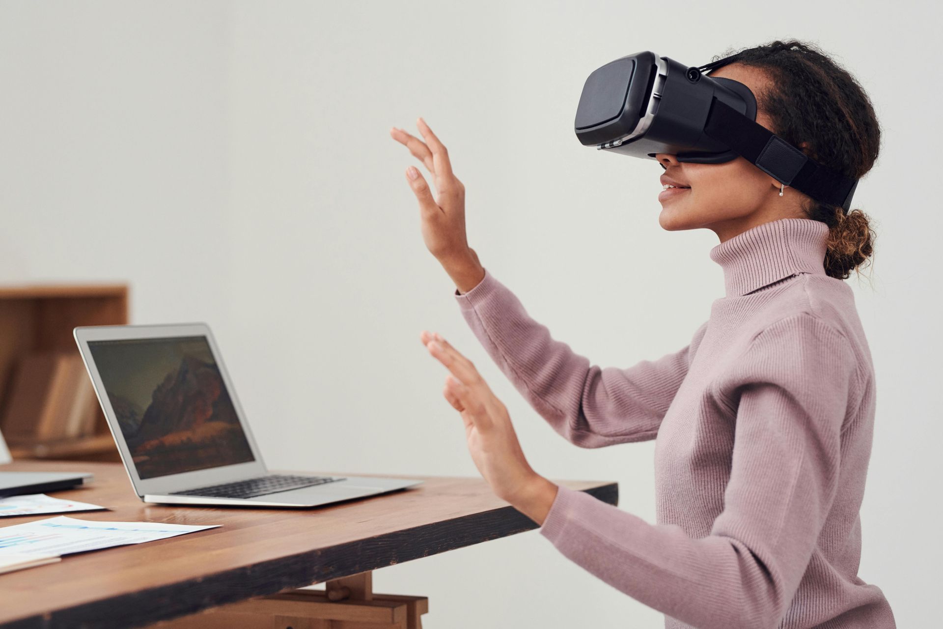 Woman wearing VR headset gestures in front of a laptop, office setting.