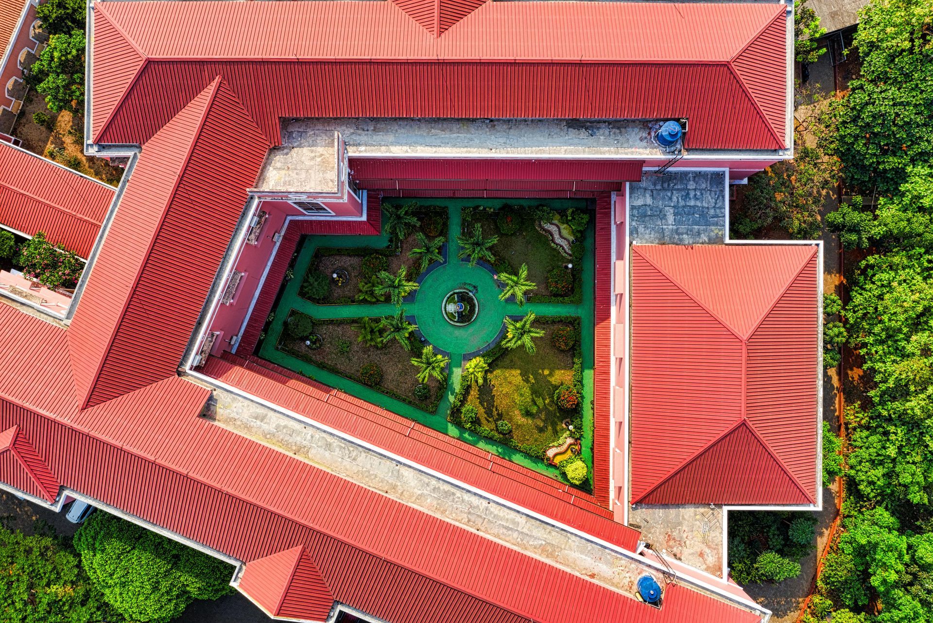 Aerial view of a building with a red tiled roof and a central garden. Green foliage surrounds the inner courtyard.
