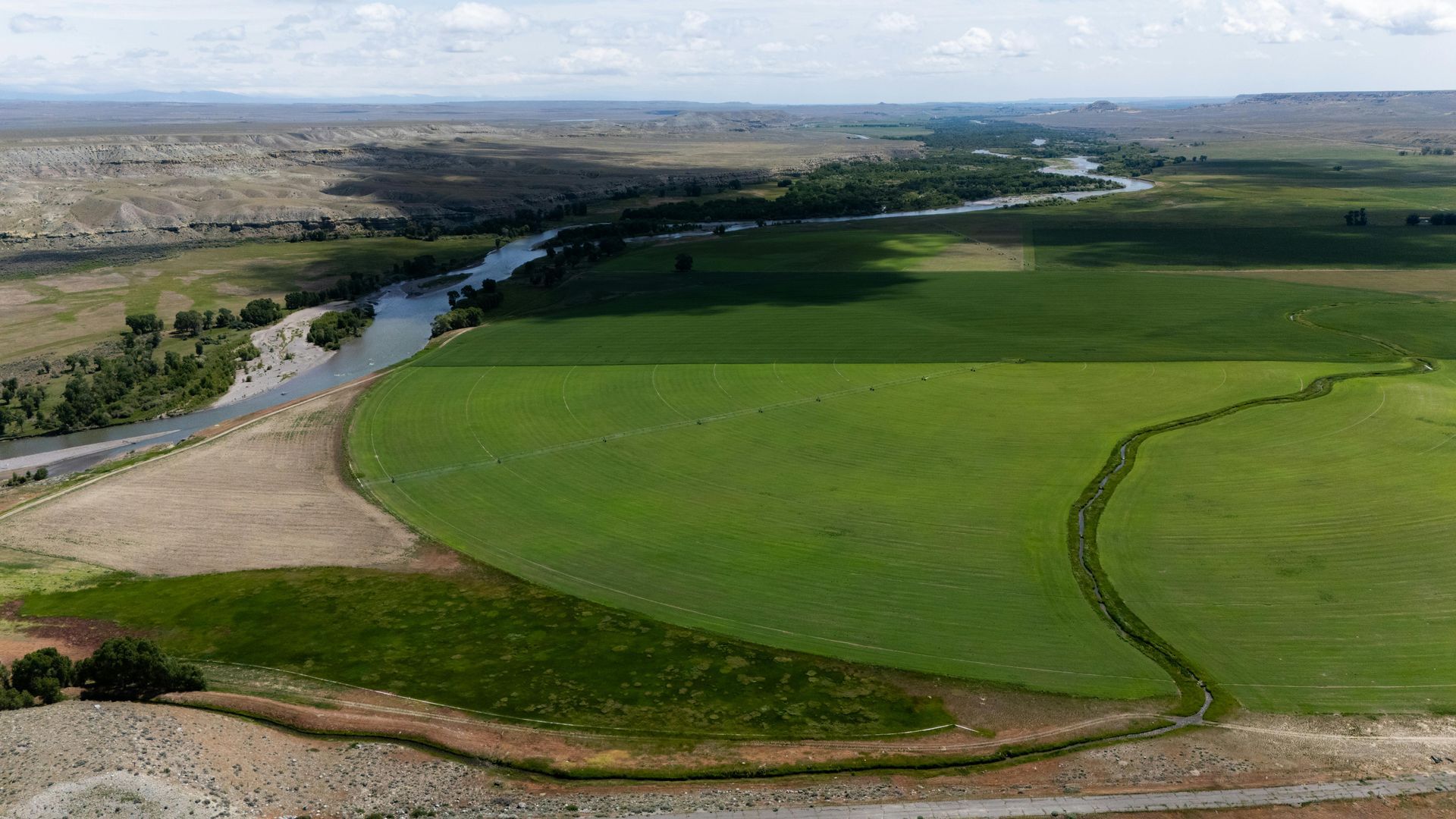 Aerial view: Green irrigated field bordered by a river, with arid hills in the distance.