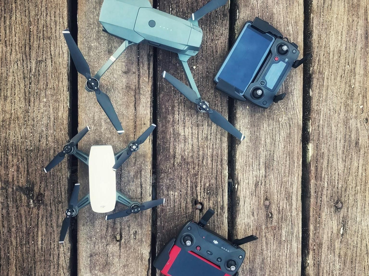 Three drones and remotes are sitting on a wooden table.