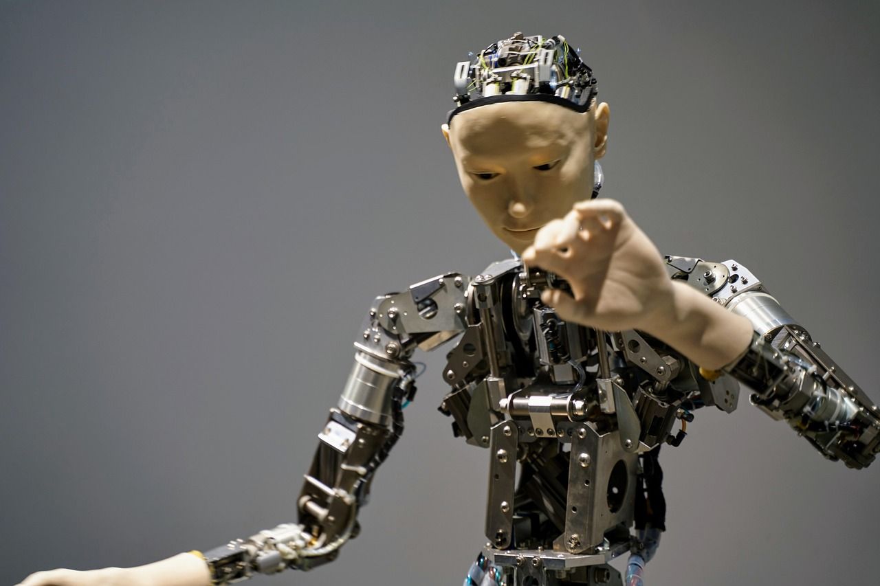 Humanoid robot with exposed mechanical components, light skin, raising arm against gray background.