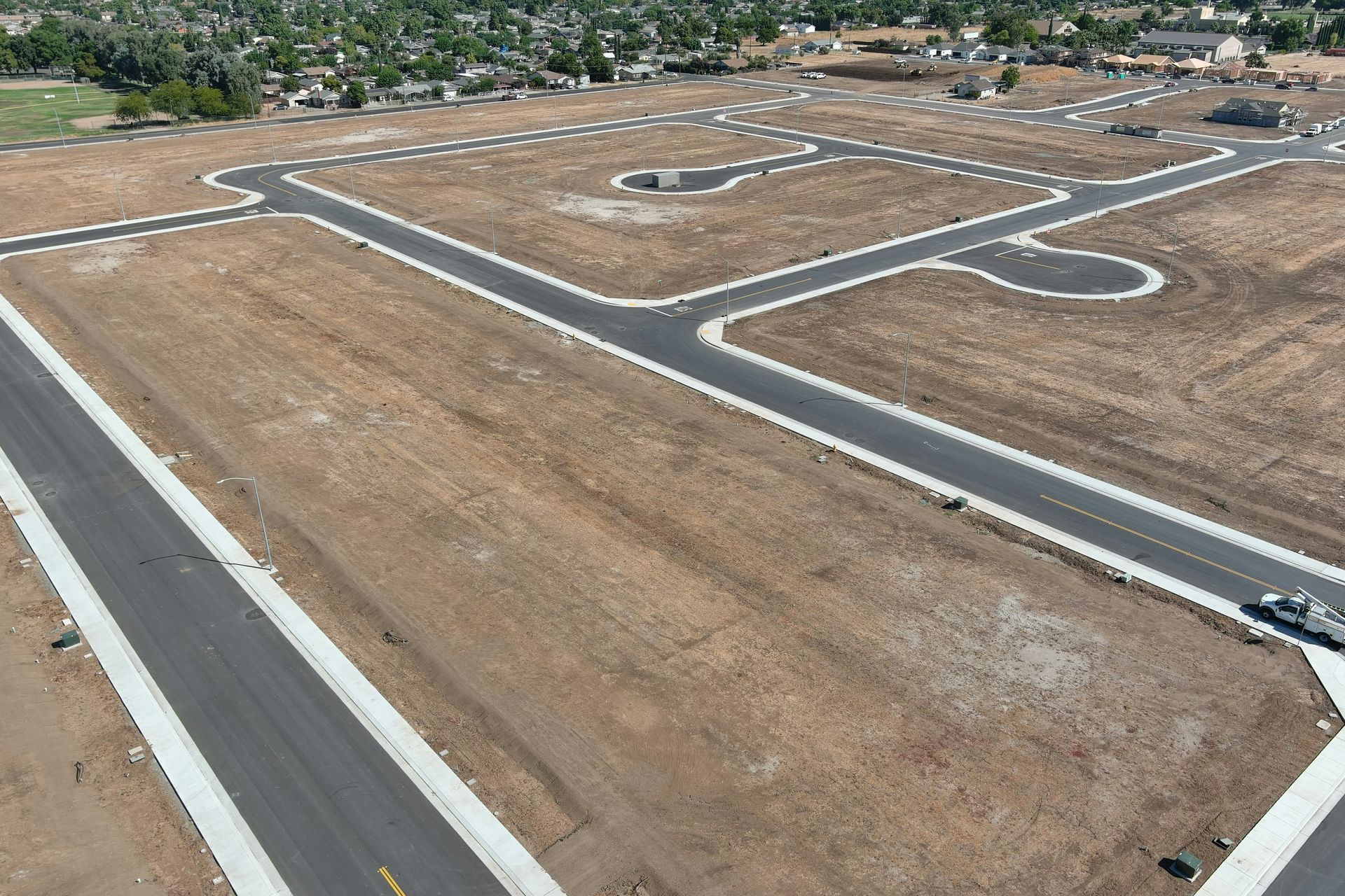 Aerial view of a new residential development with roads and plots of land, setting: dry, brown field.