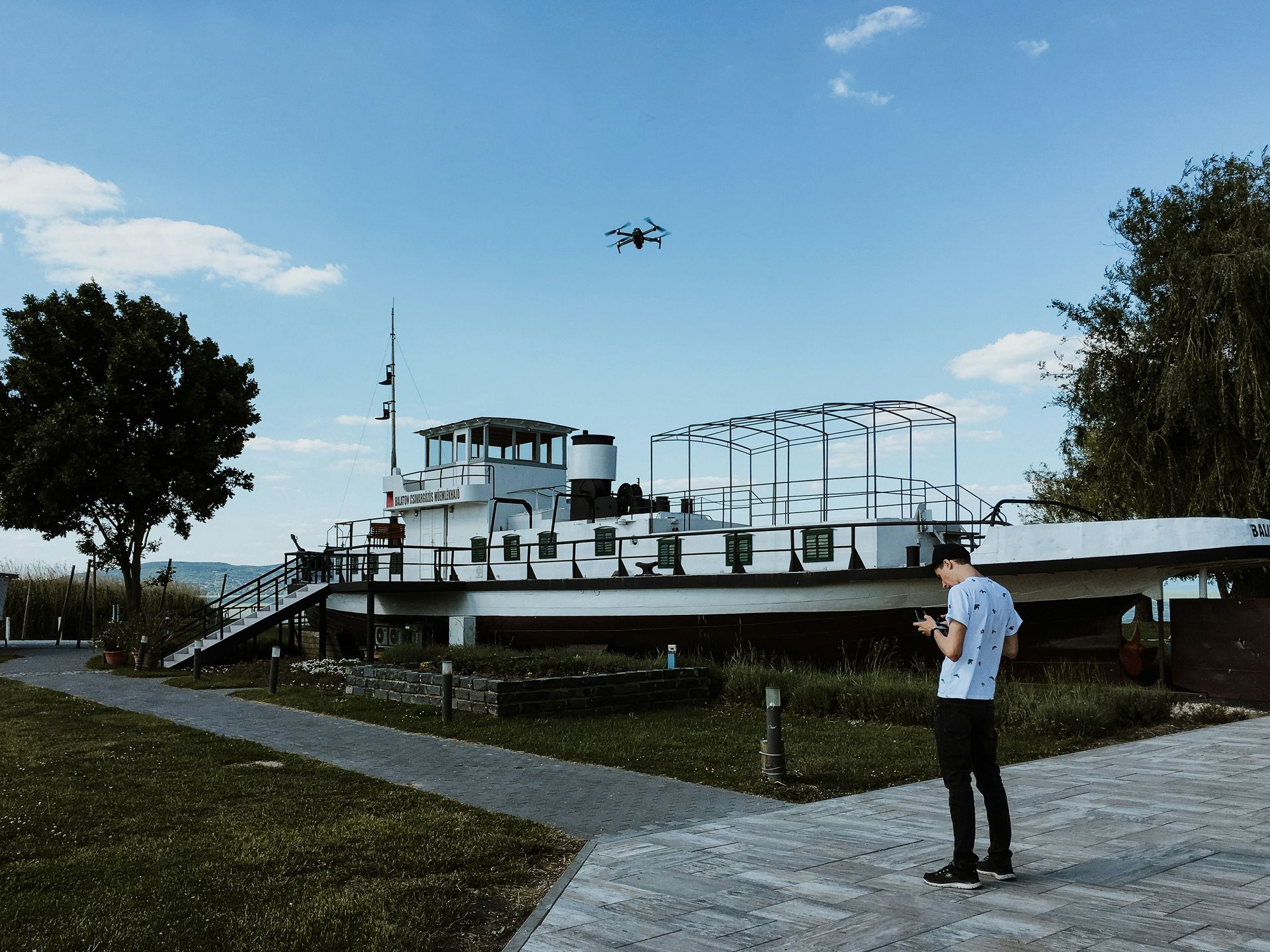 A man is standing in front of a boat with a drone flying in the background.