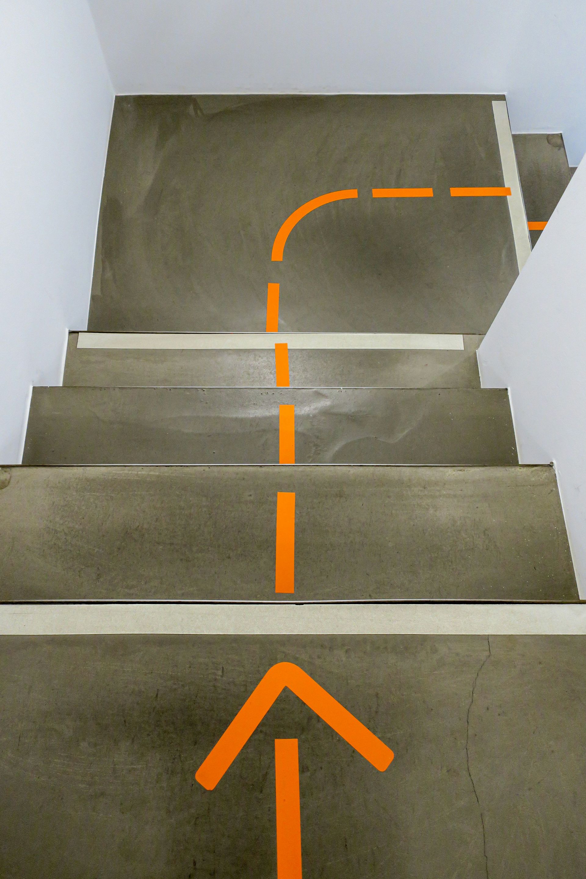 Orange arrow and dashed line painted on concrete stairs, indicating a path.