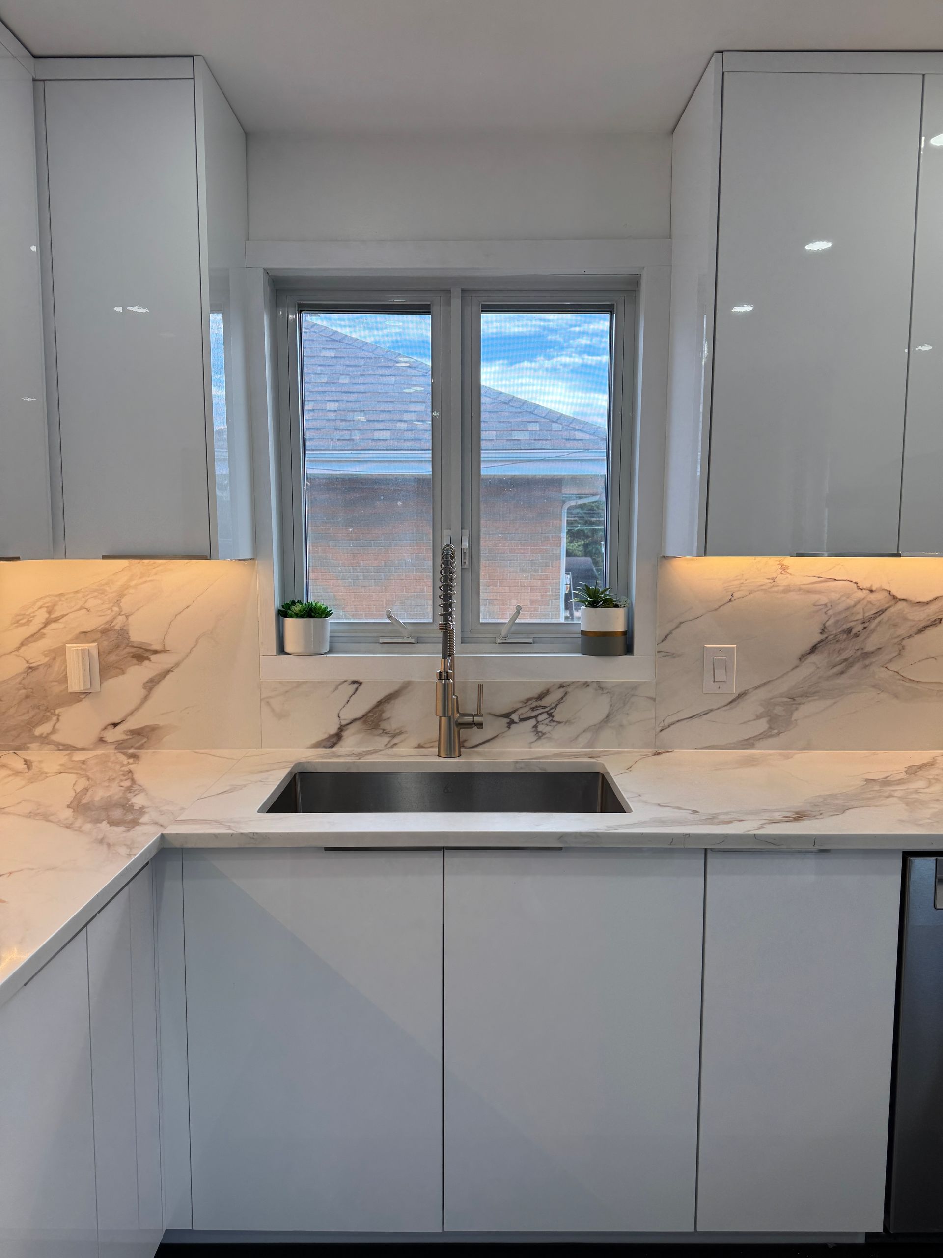 Une cuisine avec des armoires blanches, des comptoirs en marbre, un évier et une fenêtre.